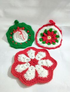 three crocheted christmas ornaments sitting on top of a white table covered in red, green and white yarn