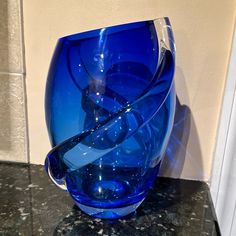 a blue glass vase sitting on top of a black marble counter next to a white wall