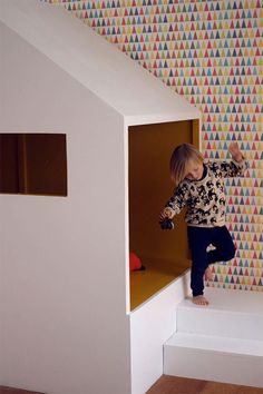 a little boy standing on top of a white step next to a wall covered in colorful triangles