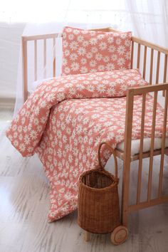 a baby crib with pink and white flowers on the bedding, next to a wicker basket