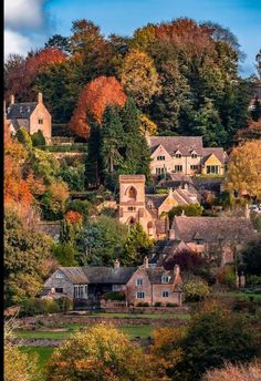 the village is surrounded by trees with autumn foliage on it's hillside and houses in the background