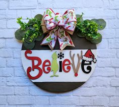 a sign that says believe on it with some plants in the corner and a bow