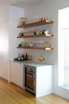 a kitchen with white cabinets and shelves filled with wine glasses, dishes, cups and vases