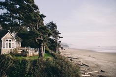 a house sitting on top of a lush green hillside next to the ocean and beach