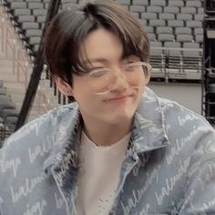 a young man with glasses sitting in front of an empty bleachers