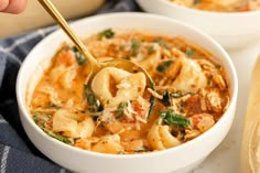 two bowls filled with pasta and spinach on top of a blue towel next to bread