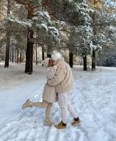 two people are walking in the snow near some trees and one person is wearing a coat