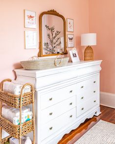 a white dresser topped with lots of drawers next to a mirror and pictures on the wall