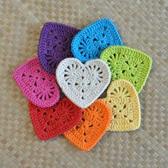 six crocheted hearts are arranged on a woven tablecloth in different colors and sizes