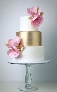 a white and gold wedding cake with pink flowers