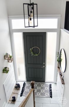 an overhead view of a hallway with a black door and white tile flooring, surrounded by hanging planters