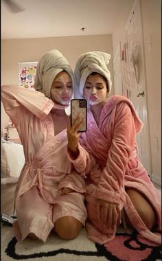 two women in robes are taking a selfie with their cell phone while sitting on the floor