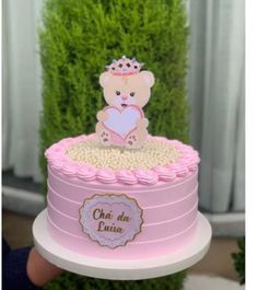 a pink cake with a teddy bear on top is being held up by a person