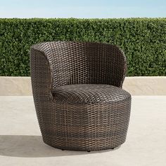 a brown wicker chair sitting on top of a cement floor next to a hedge