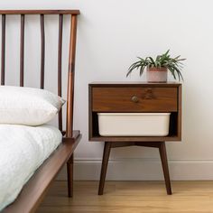 a nightstand with a potted plant on it next to a bed