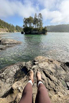 someone is sitting on the rocks by the water with their feet up in the air