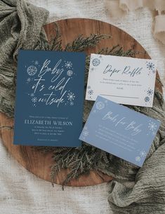 the wedding stationery is laid out on a wooden platter with greenery and snowflakes