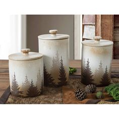 three canisters with trees painted on them sitting on a table next to pine cones