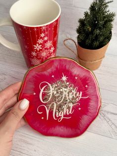 a hand holding a red plate with the words merry night on it next to a coffee mug