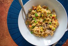 a white bowl filled with rice and meat on top of a blue plate next to a fork