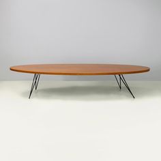 an oval wooden table with black legs on a white floor in front of a gray wall