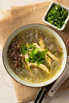 a white bowl filled with soup next to some chopsticks and a container of greens