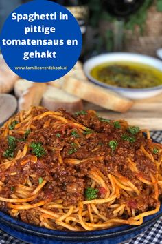 a blue plate topped with spaghetti and meat next to bread on a checkered table cloth