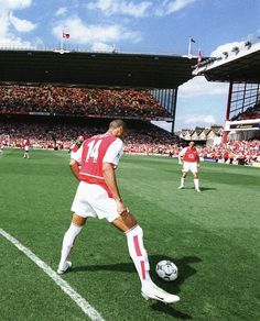 a man kicking a soccer ball on top of a lush green field in front of a crowd