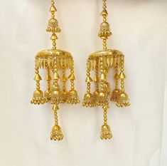 two gold earrings hanging from a white curtain