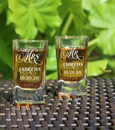 two shot glasses with mr and mrs engraved on them sitting in front of green leaves