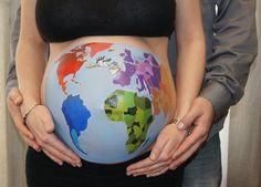 a pregnant woman holding her belly painted in the colors of the world