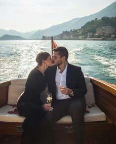 two people sitting on a boat kissing and holding glasses of wine in front of them