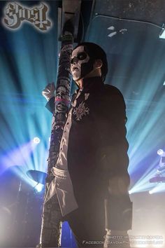 a man in black jacket and mask holding up a pole with lights behind him on stage