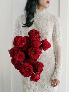 a woman in a white dress holding a bouquet of red flowers with her hands behind her back