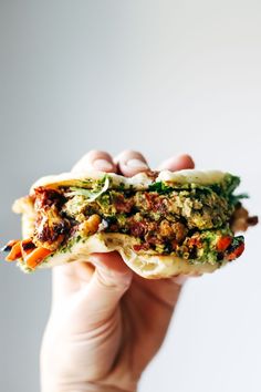 a hand holding a sandwich with meat and veggies on it in front of a white background