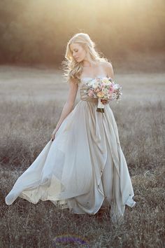 a woman in a dress is walking through the grass with her bouquet on her shoulder