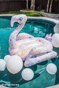 an inflatable flamingo float floating on top of a pool surrounded by balloons