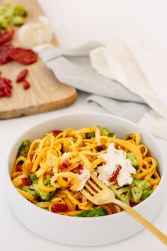 a pasta dish with broccoli, cheese and bacon in a white bowl next to a cutting board