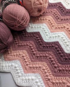 two balls of yarn sitting on top of a crocheted blanket next to each other