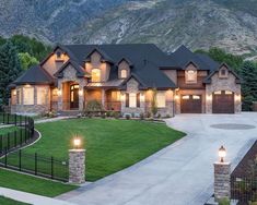 a large house with lights on in the front yard and mountains in the back ground