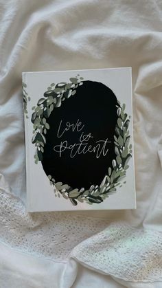 a card with the words love is patient written in white ink on top of a black circle surrounded by greenery