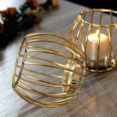 two gold wire candle holders sitting on top of a wooden table next to each other