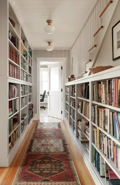 a long hallway with many bookshelves and rugs on the floor in front of it