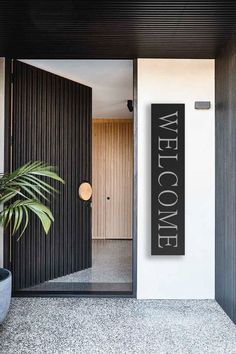 a welcome sign on the front door of a modern house with black and white walls