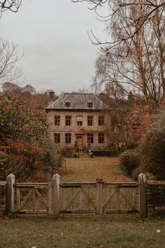 an old brick house surrounded by trees and bushes in the fall with leaves on the ground