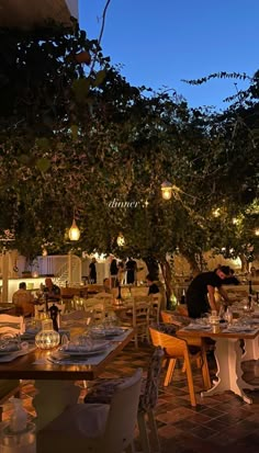 an outdoor dining area with tables and chairs at night, lit by hanging lights from the trees