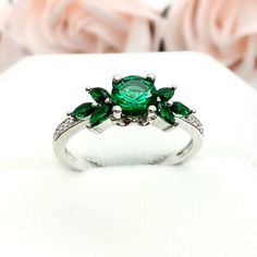 This beautiful ring is made from genuine 925 sterling silver with rhodium plating. Ring details- -The Main stone is a round cut 6mm Lab Created Emerald Stone -Side stones are 4mm by 2mm Lab Emerald Marquise and 1mm Round simulated diamonds -Ring is casted in solid 925 sterling silver with rhodium plating (yellow gold and rose gold plated also available, please check the drop down menu for more options) -The Total face height of the ring measures 7mms and the band width measures 1.5mms -Each ring Green Cubic Zirconia Cluster Promise Ring, Silver Emerald Open Ring For Promise, Silver Emerald Open Ring With Center Stone, Silver Emerald Ring With Center Stone, Open Ring Style, Sterling Silver Emerald Ring For Promise, Green Open Cluster Ring For Promise, Silver Rings With Accent Stones For May Birthstone, Elegant Green Flower Ring In Sterling Silver, Fine Jewelry Flower Ring With May Birthstone