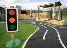 a traffic light sitting on the side of a road next to a playground area with fake grass