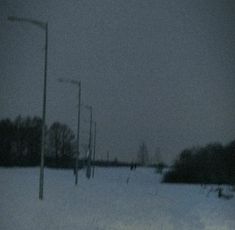 a blurry photo of snow covered ground with street lights in the distance and people walking on it