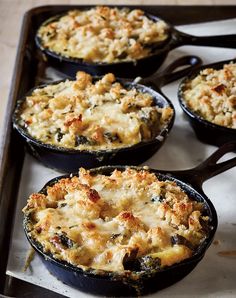 four cast iron skillets filled with different types of casseroles on a baking sheet